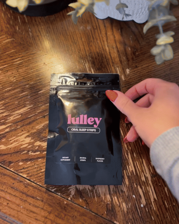Hand holding a package of 'lulley' oral sleep strips on a wooden table.