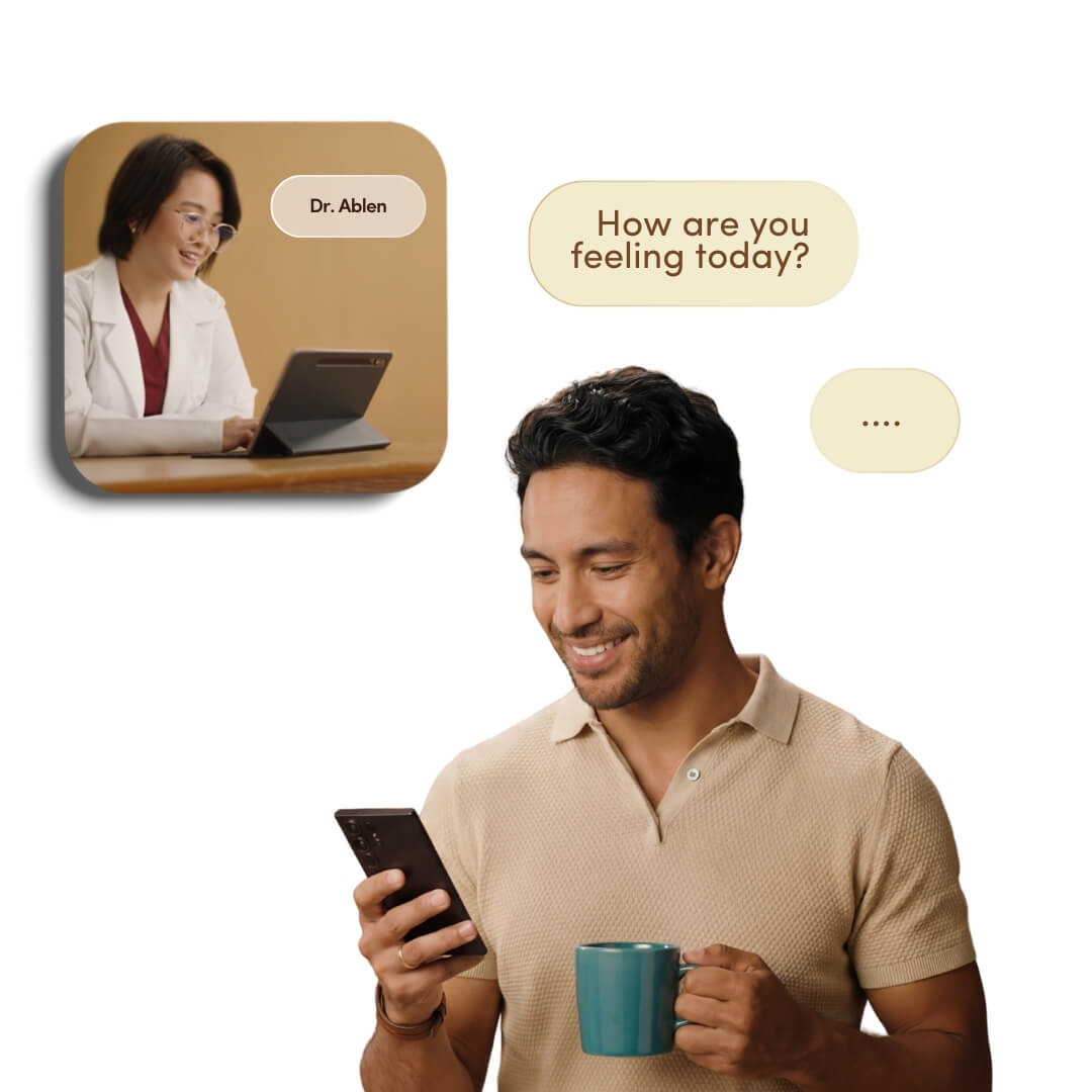 A man smiles while using his phone for a telehealth consultation with a doctor, holding a mug.
