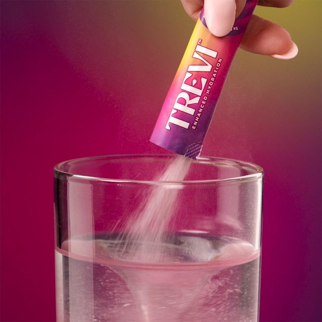 Pouring a powdered drink mix into a glass of water.