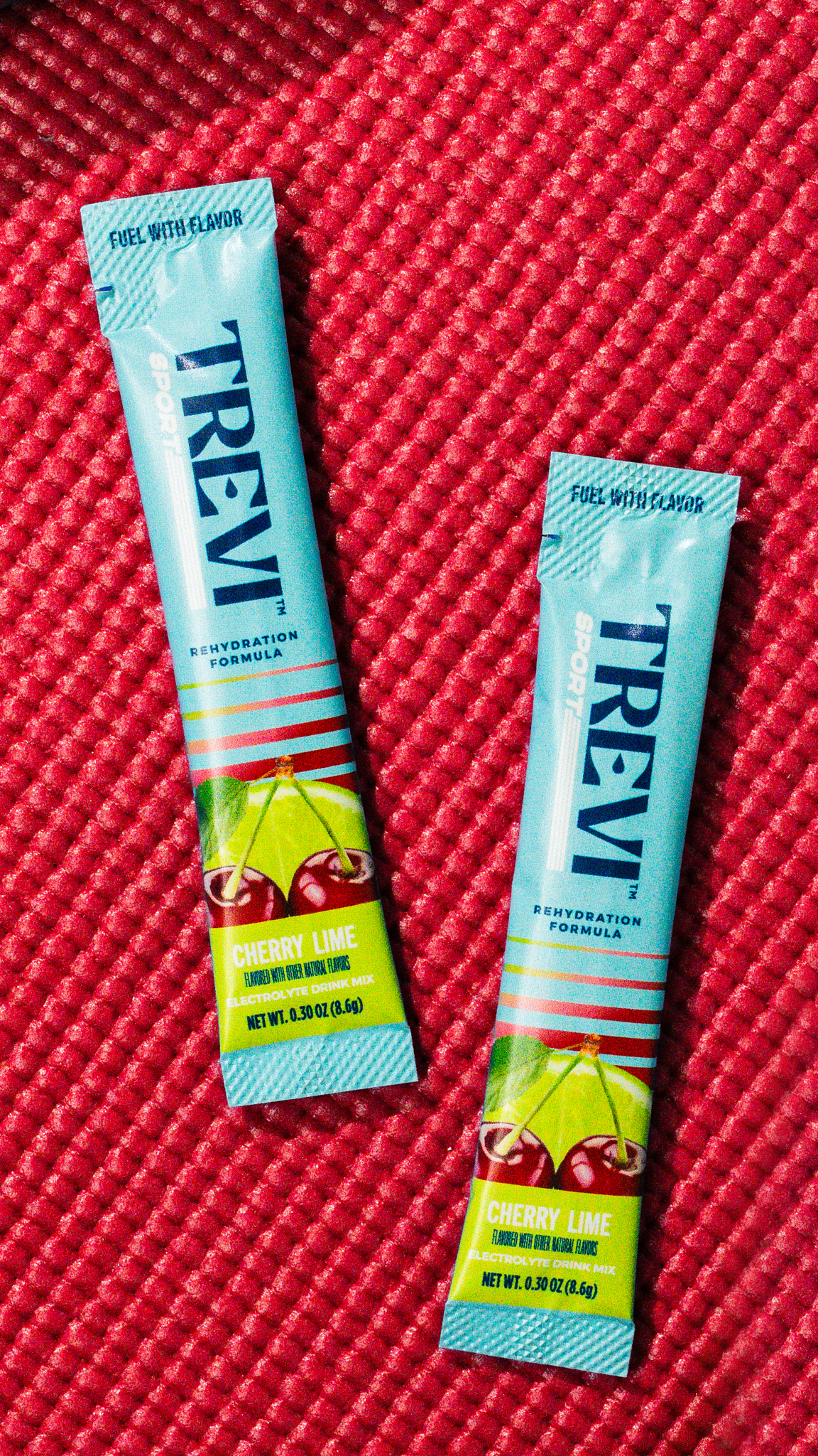 Two packets of Trevi Sport Cherry Lime rehydration formula lie on a textured red surface.