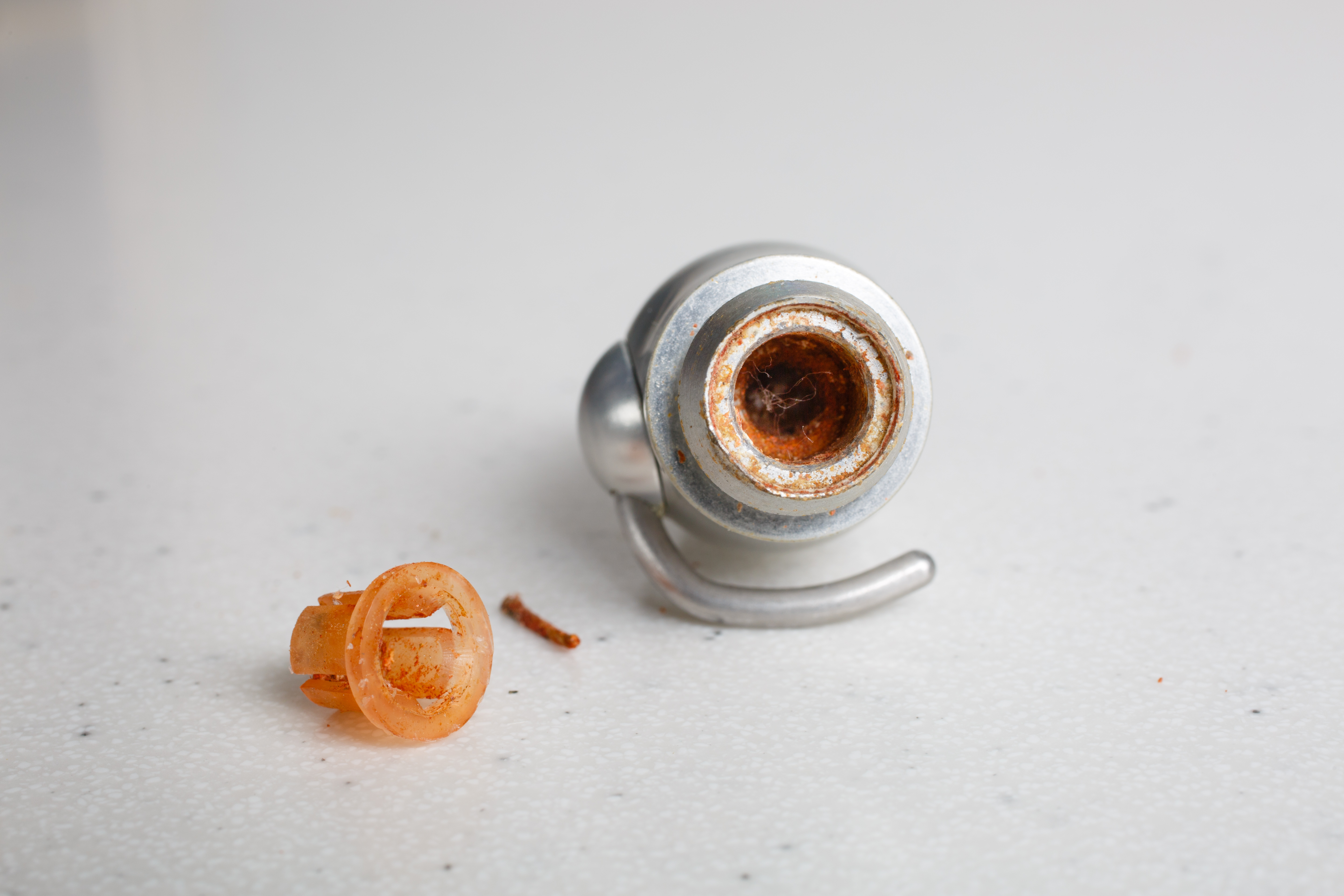 Close-up of a rusty metal object and an orange plastic piece on a white surface.