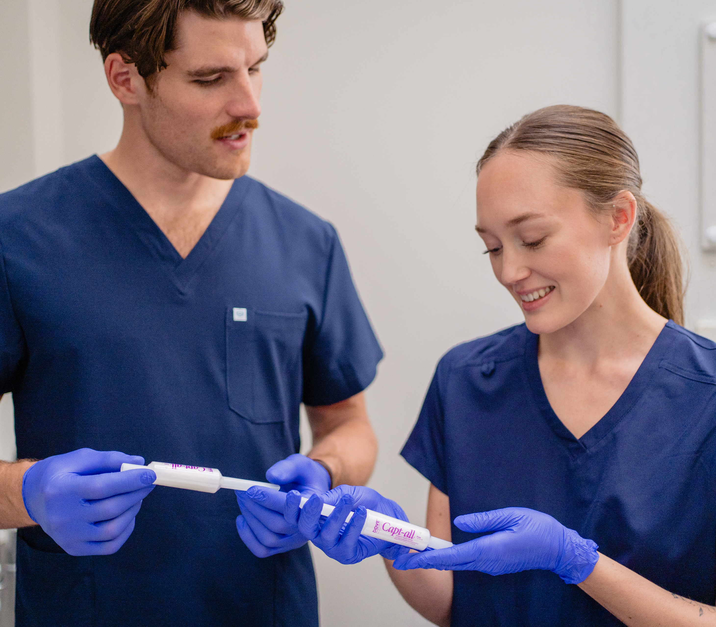 Two people in blue scrubs examining a medical tool.