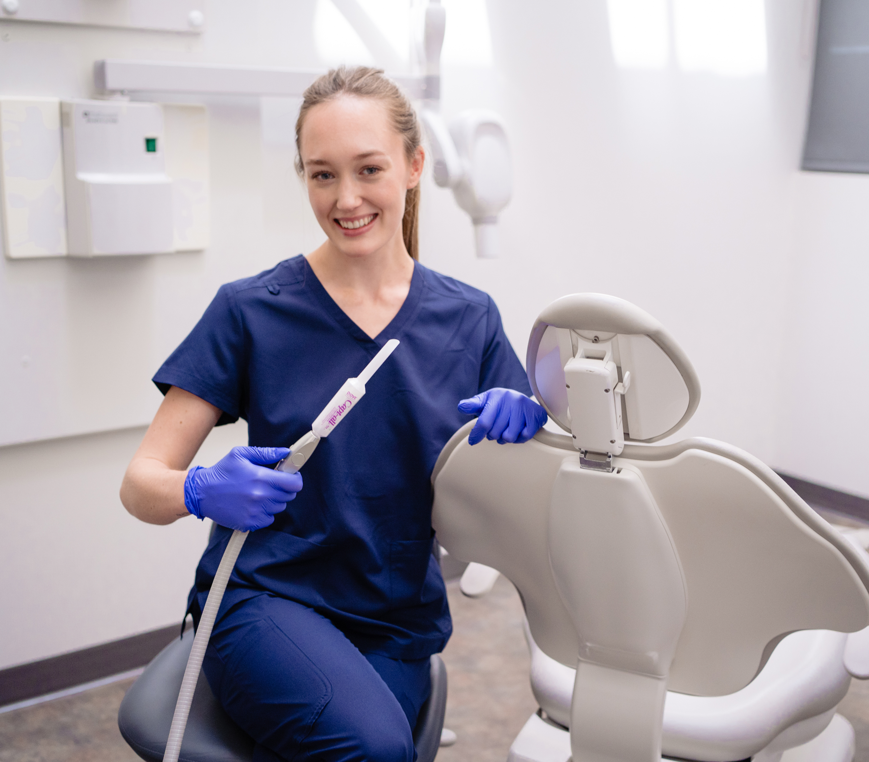 Smiling dental professional in scrubs holding a dental tool in a clinic.
