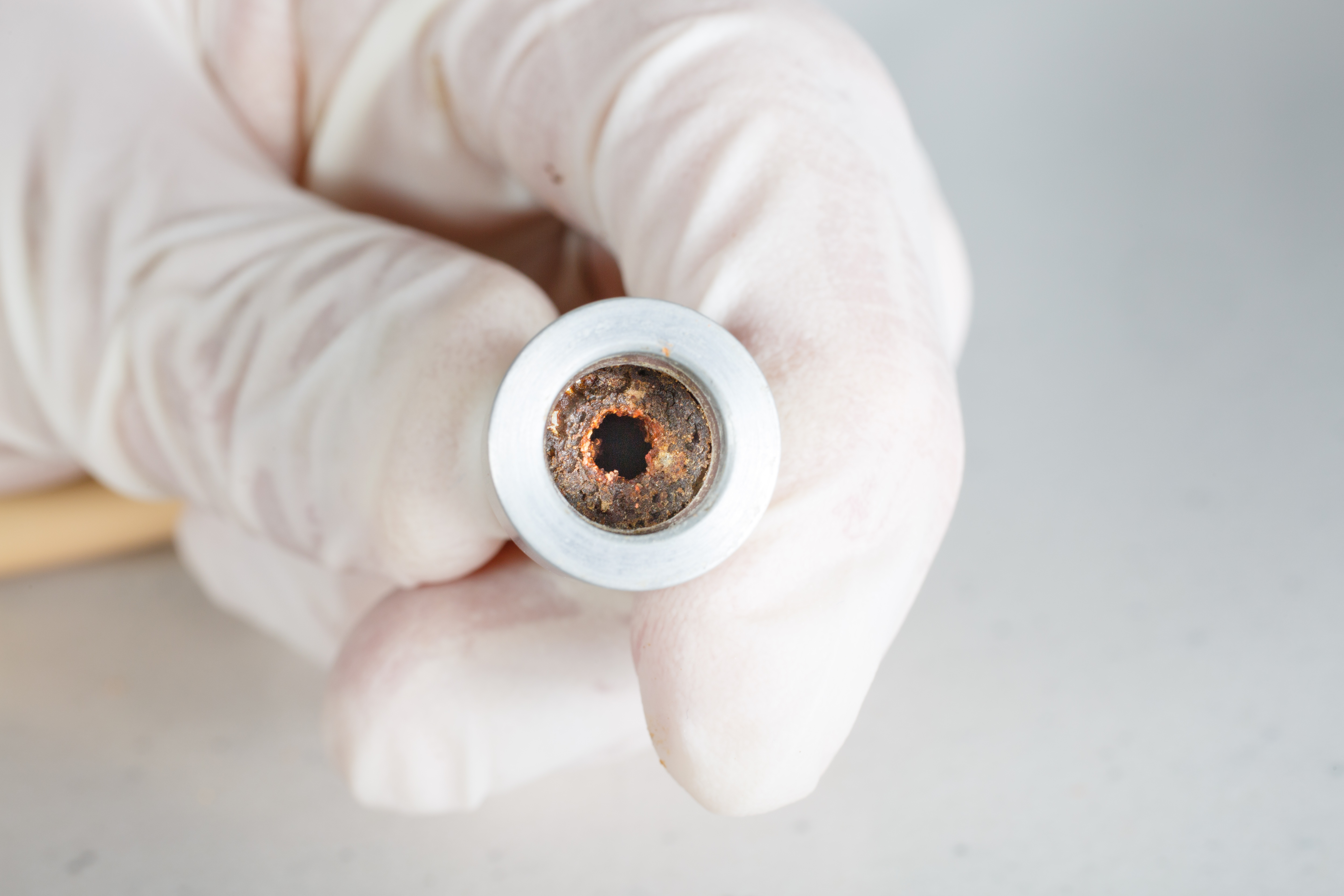 Gloved hand holding a corroded metal pipe with a visible hole.