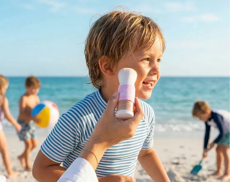 An adult applies bug repellent from a roll-on bottle to a young boy's arm outdoors.