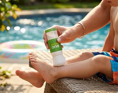 An adult uses a Bug Brush applicator to apply powder to a child's lower leg by a pool.