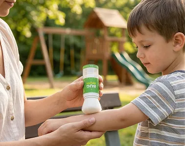 An adult applies bug repellent from a roll-on bottle to a young boy's arm outdoors.