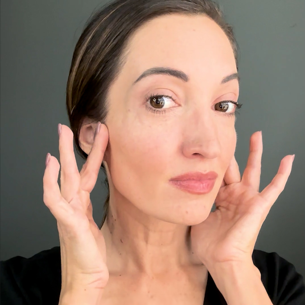 Woman touching her face with both hands against a gray background.