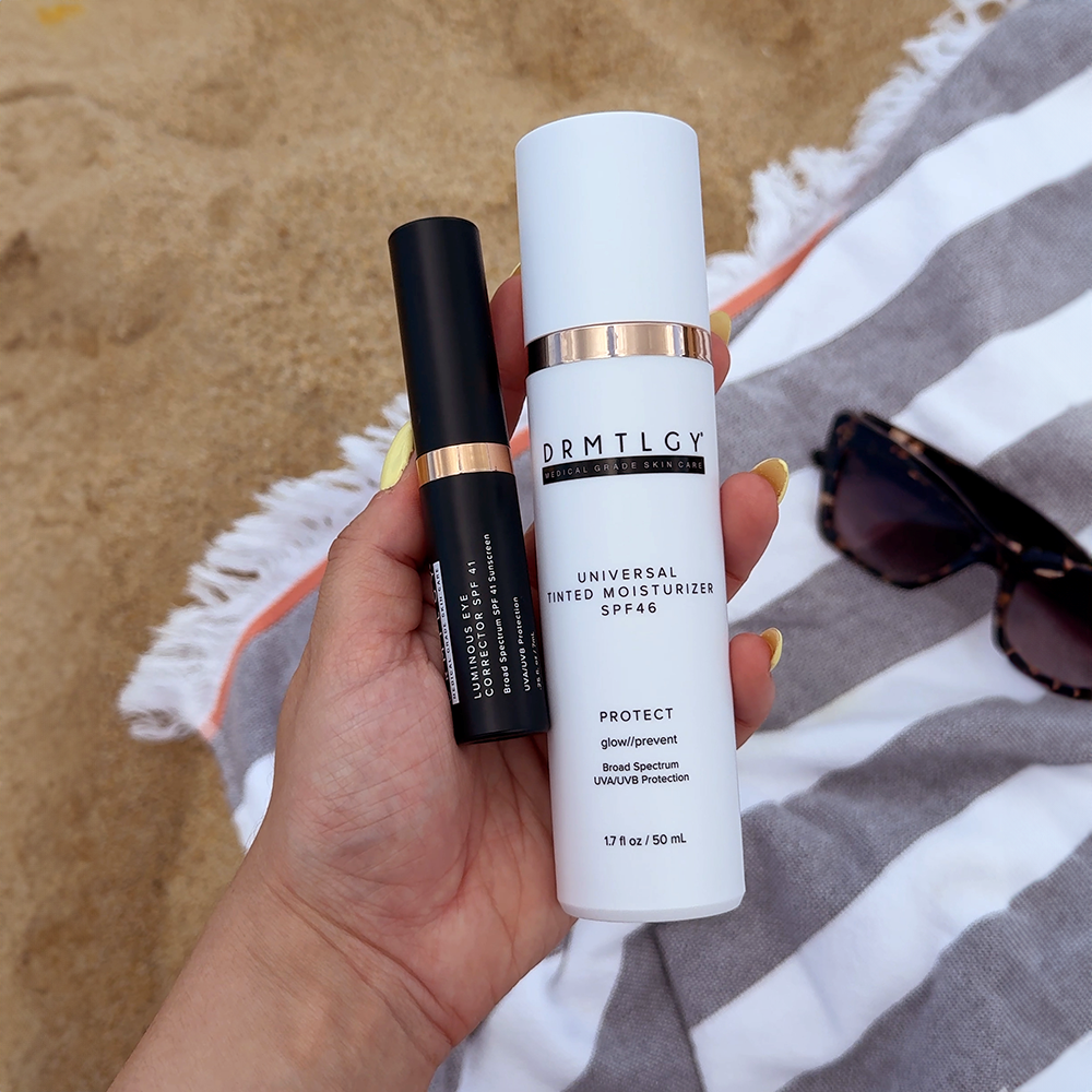 Hand holding skincare products on a beach towel with sunglasses nearby.