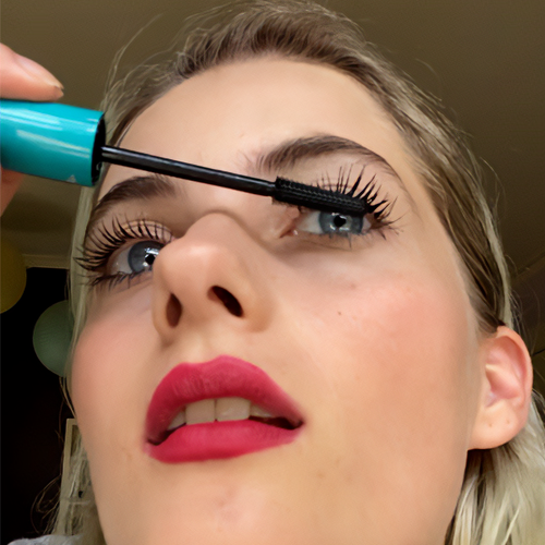 Person applying mascara to eyelashes with a blue mascara wand.