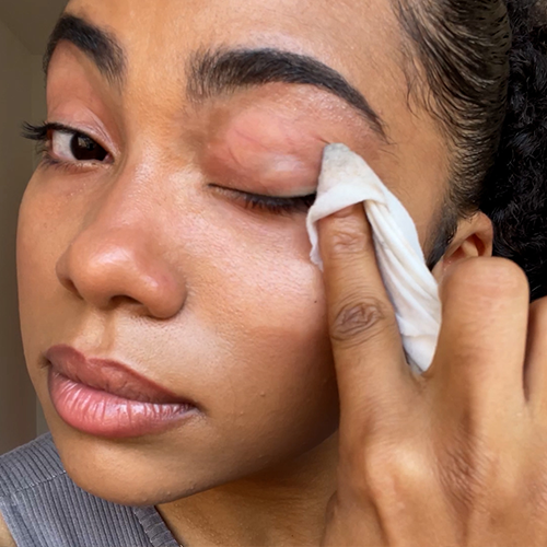 Person using a cloth to remove makeup from their eyelid.