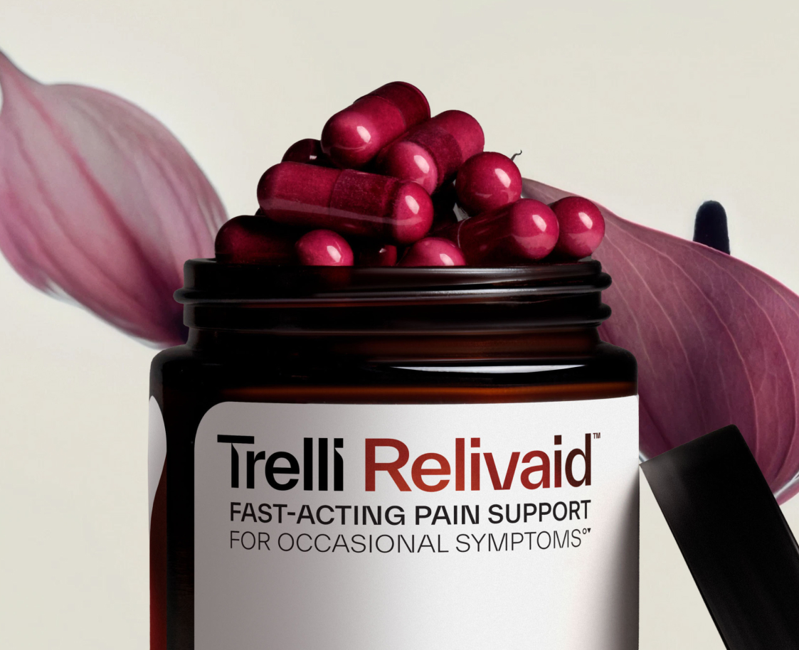 A bottle of Trelli Relivaid fast-acting pain support overflowing with dark pink capsules, with flower petals behind it.
