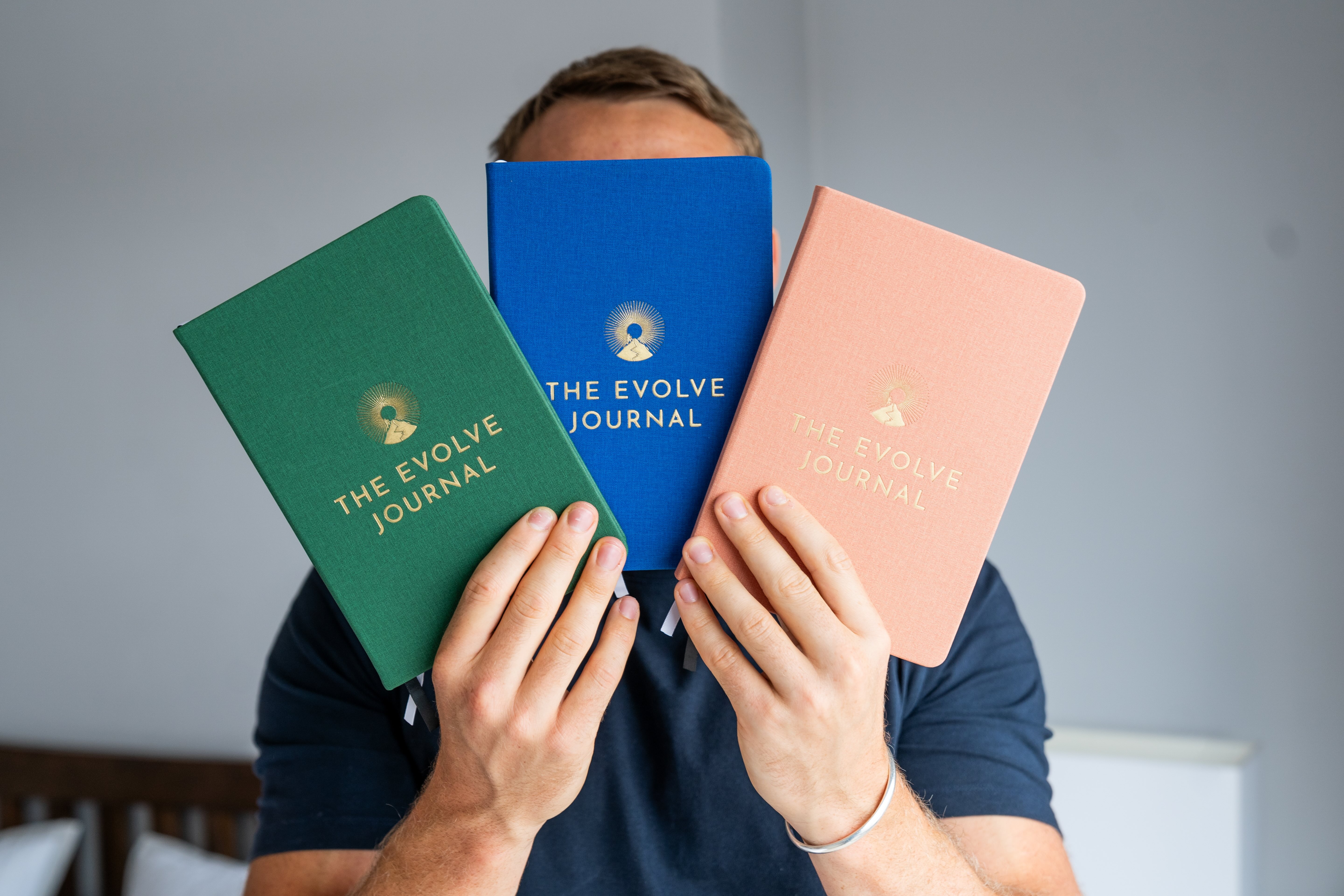 Person holding three journals in green, blue, and pink covers.
