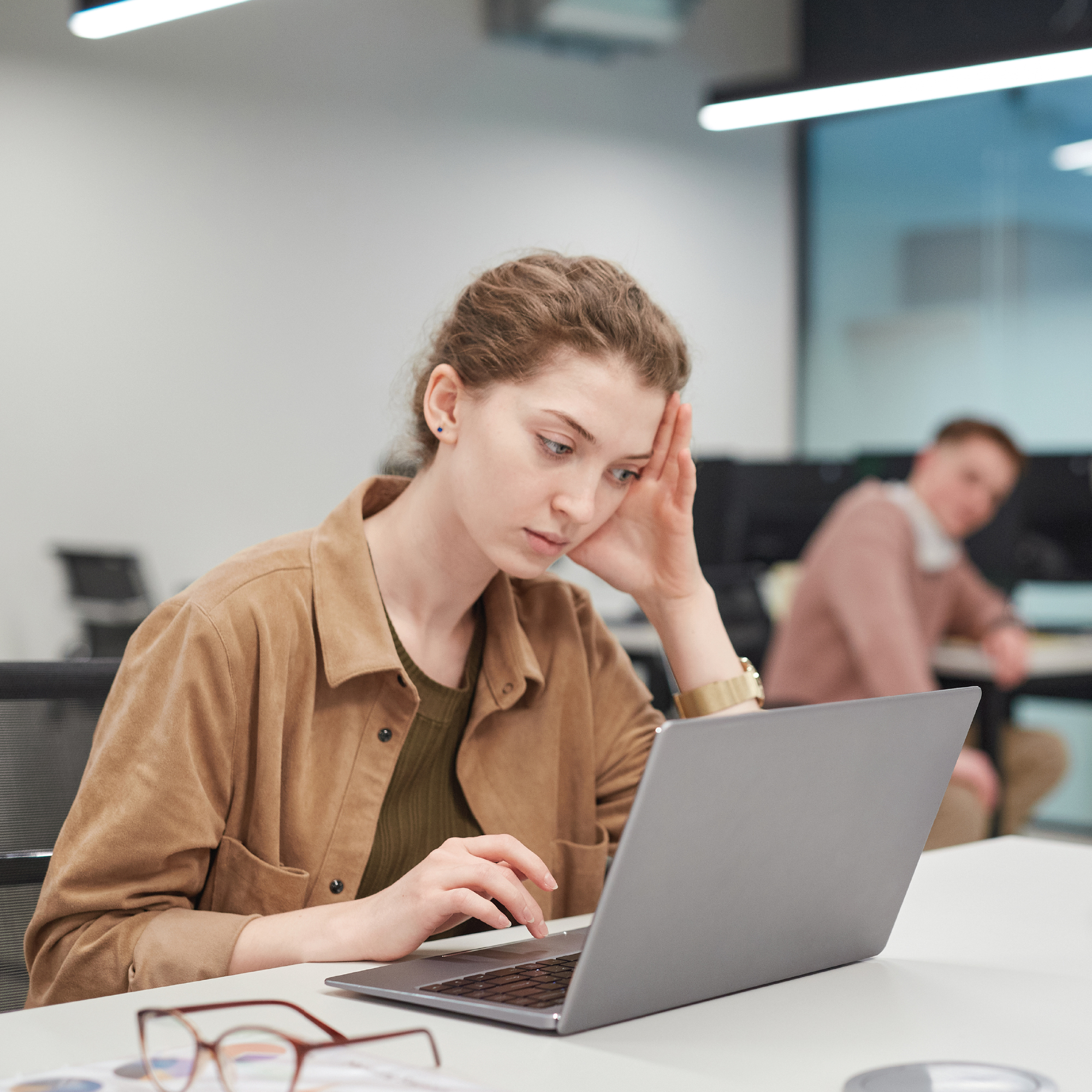 Person looking at a laptop screen, appearing thoughtful, in an office setting.