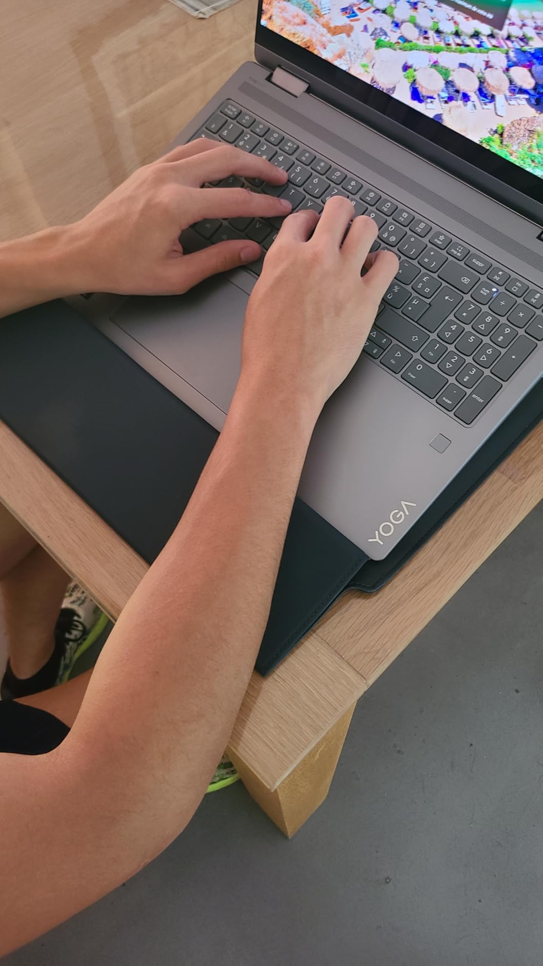 Hands typing on a Lenovo Yoga laptop on a wooden table.