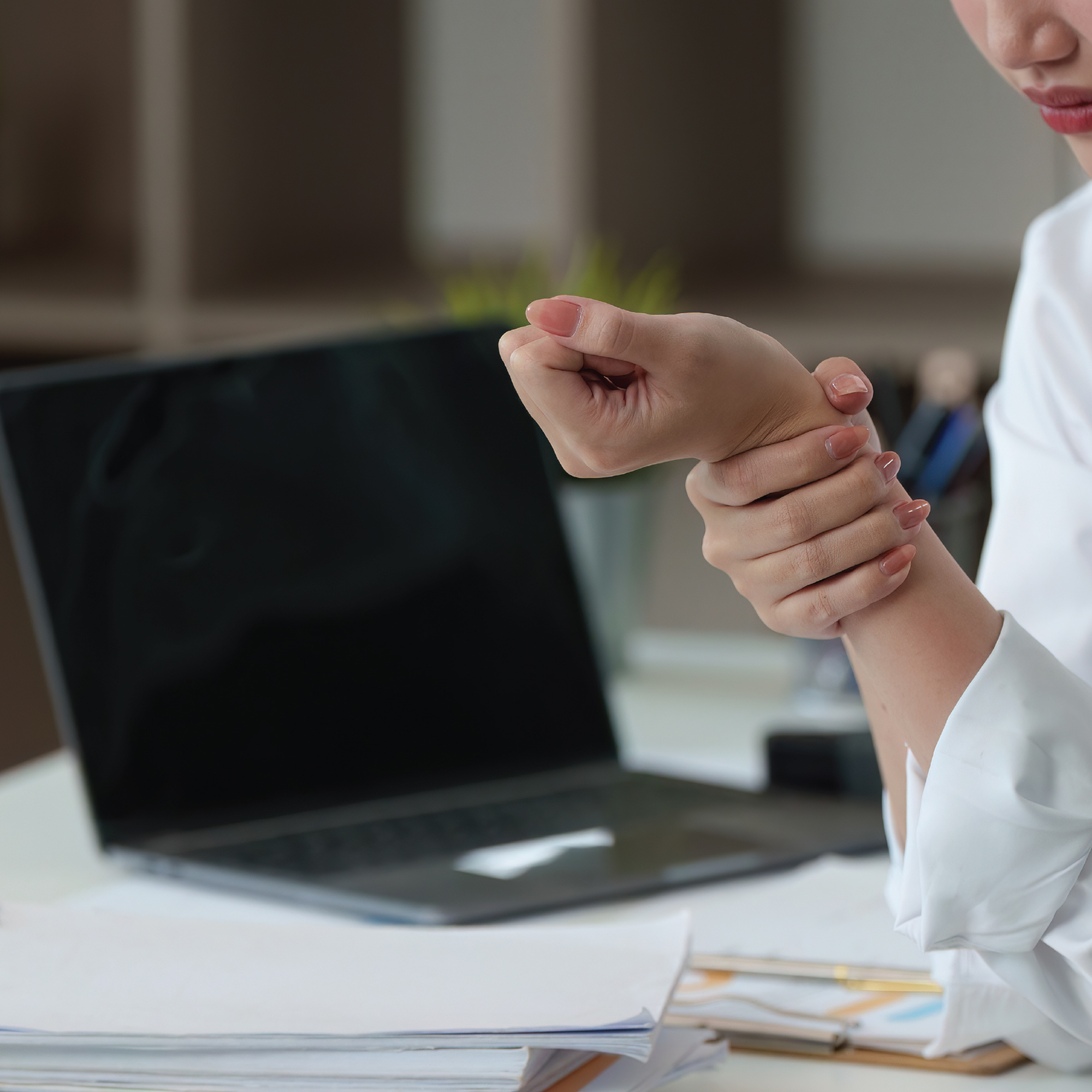 Person holding their wrist near a laptop on a desk.