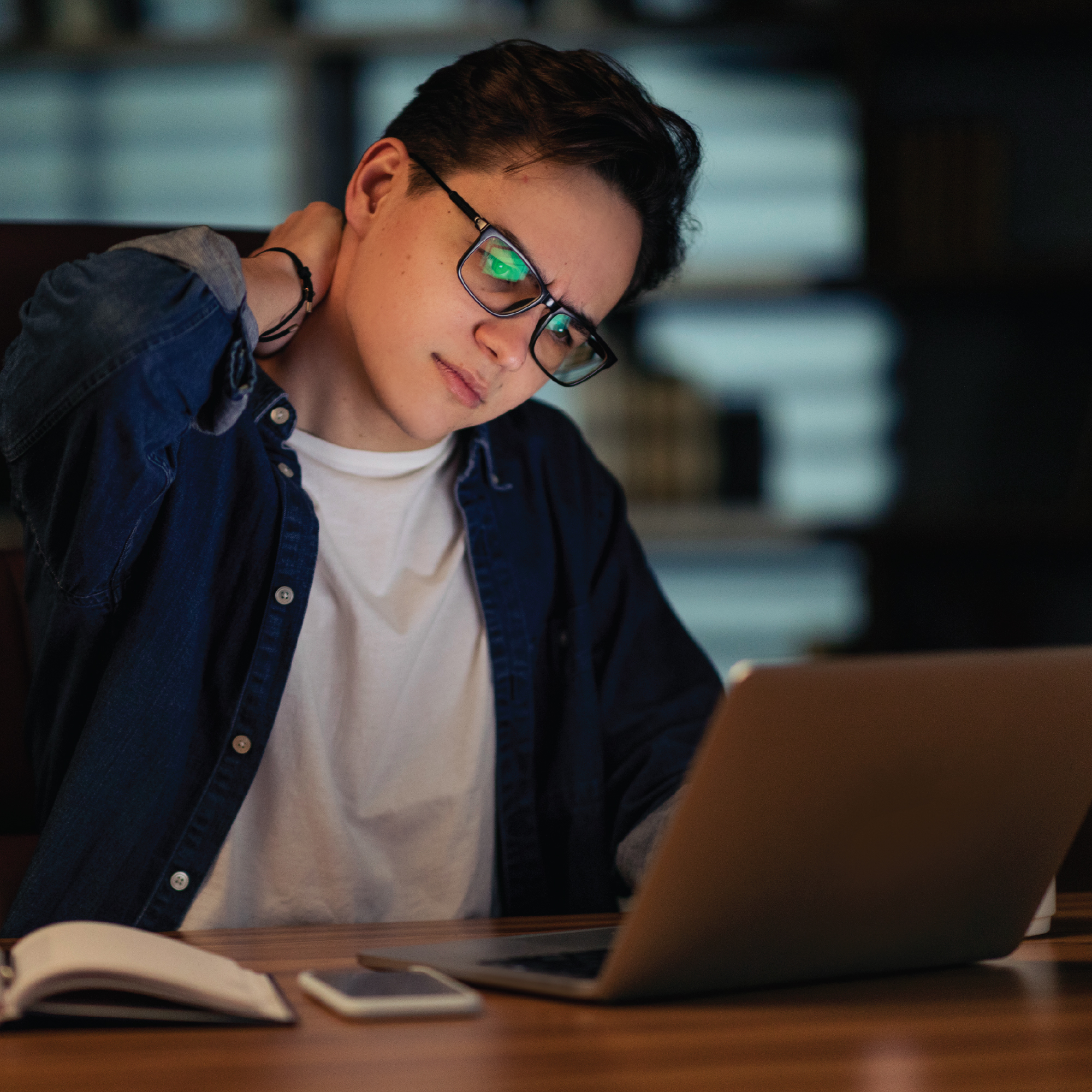 Person with glasses using a laptop, rubbing neck.