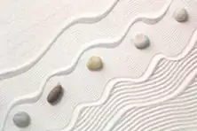 Smooth stones on white sand that has been raked into flowing, wavy patterns.