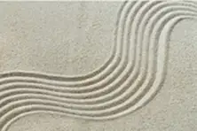A close-up of a zen sand garden with a flowing, wavy pattern raked into the sand.