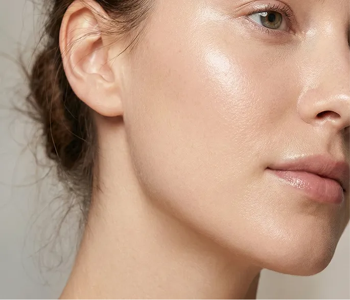 A close-up of the side of a woman's face showing her clear, glowing skin, ear, and mouth.