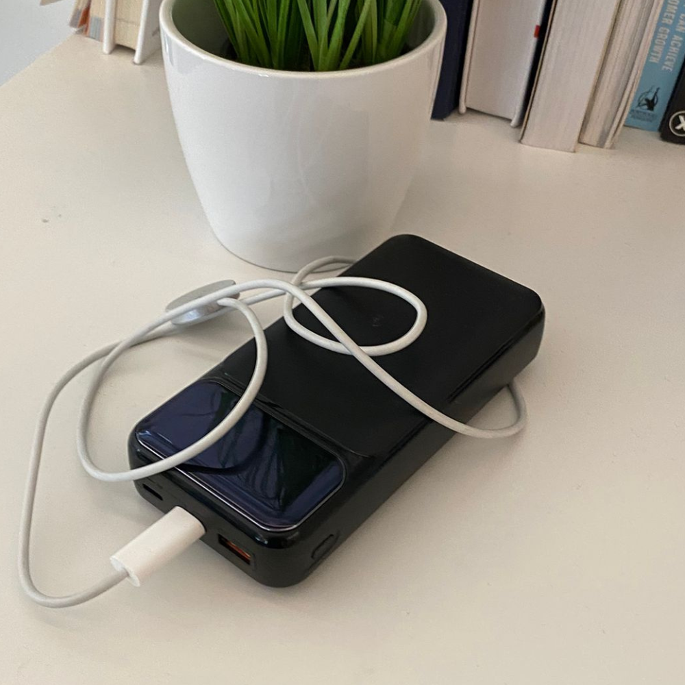 A smartphone and charger on a table next to a potted plant and books.