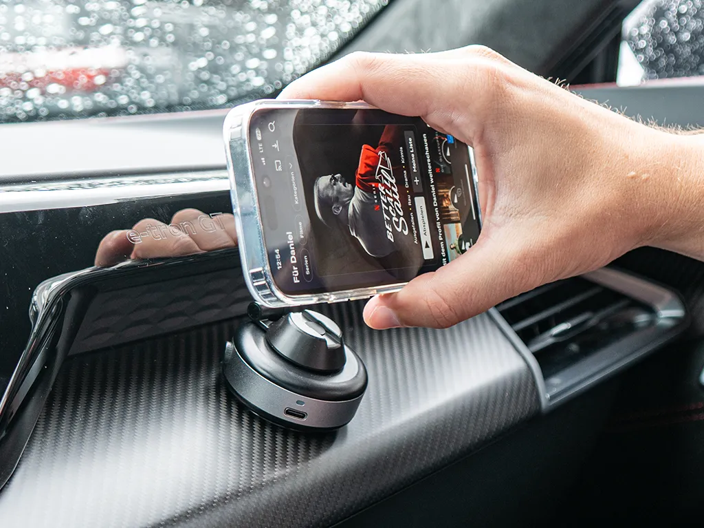 Hand holding a smartphone near a car dashboard with a magnetic phone mount.
