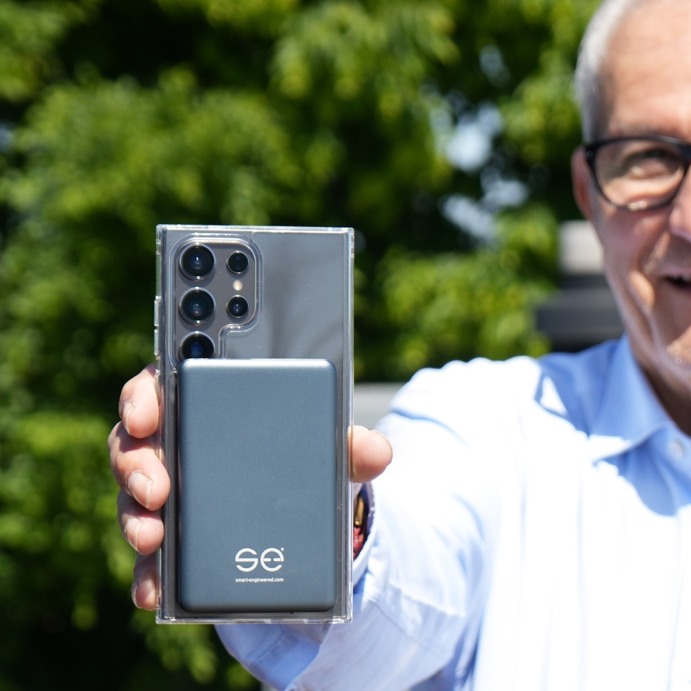 Person holding a smartphone with a camera and attached device outdoors.