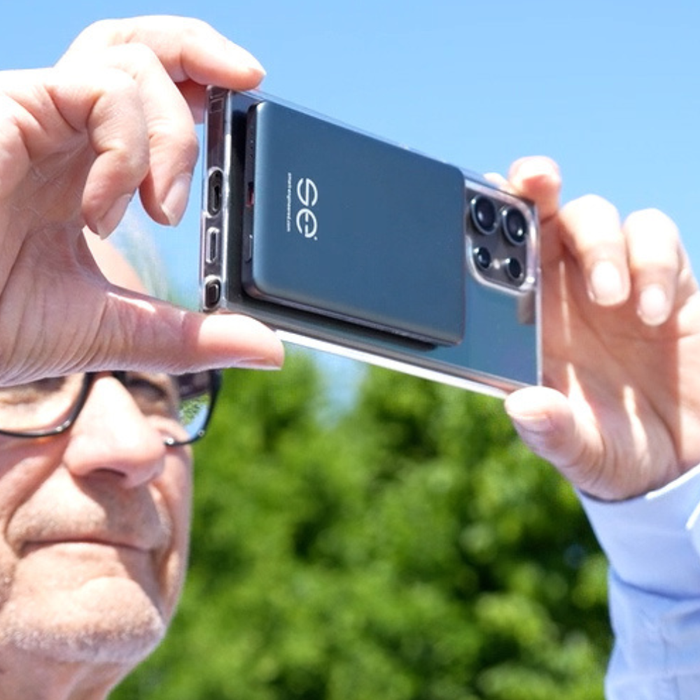 Person holding a smartphone with a camera attachment outdoors.