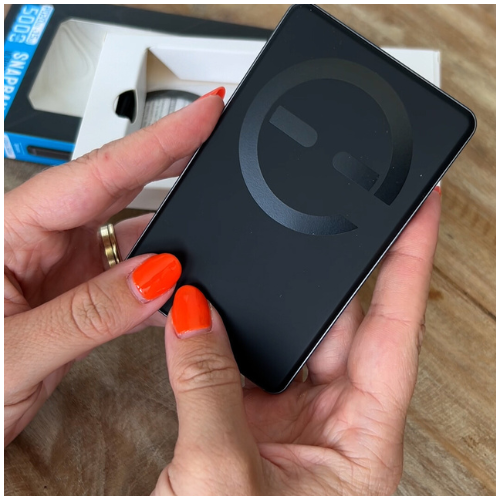 Person holding a black external hard drive with packaging in the background.