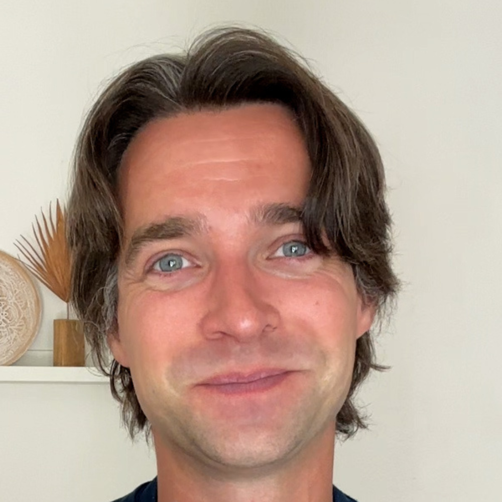A person with brown hair smiling in a light-colored room.