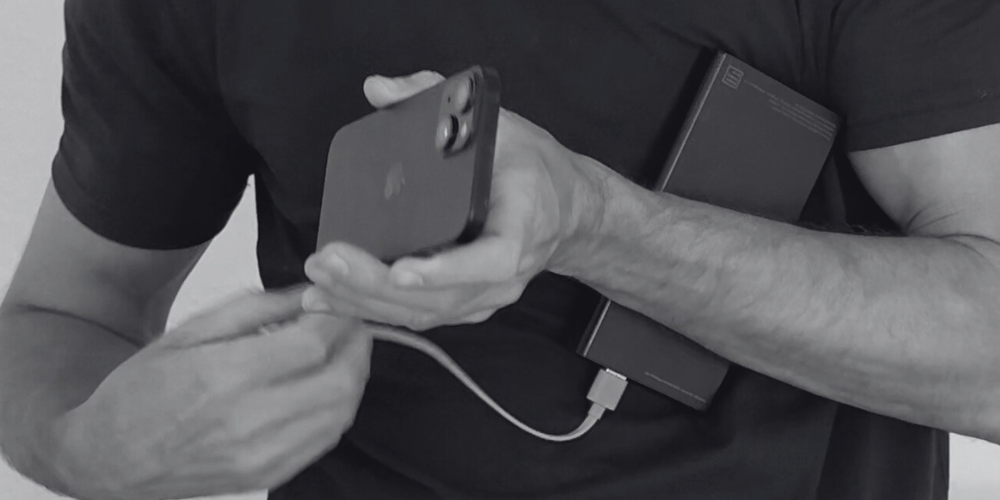 Person holding a smartphone and power bank, connecting them with a cable.
