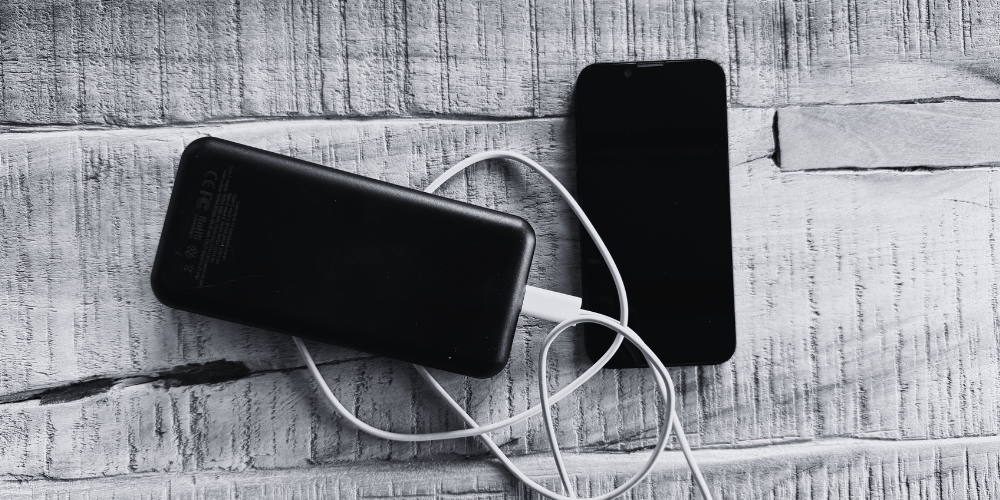 Black power bank and smartphone connected by a white cable on a wooden surface.