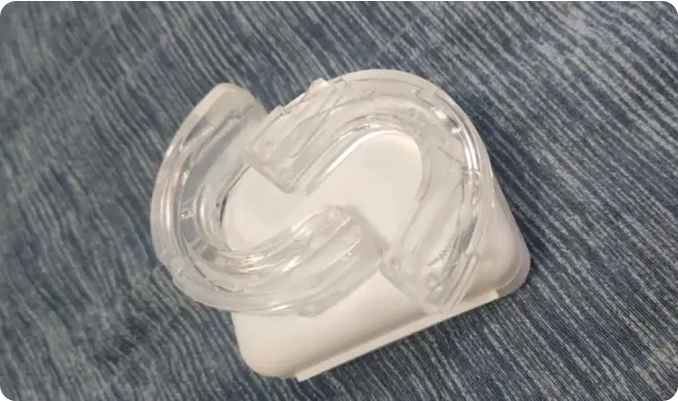 Clear mouthguard on a white case, placed on a blue fabric surface.