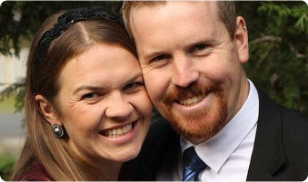 A smiling couple posing closely outdoors.