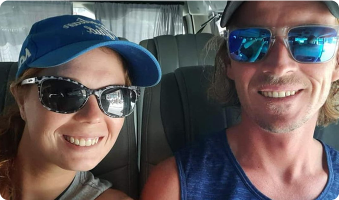 A smiling couple wearing sunglasses and baseball caps in a vehicle.