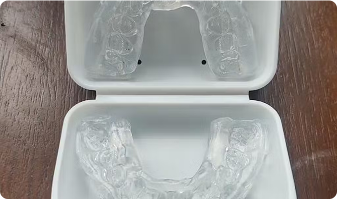 Clear dental aligners in a white case on a wooden surface.