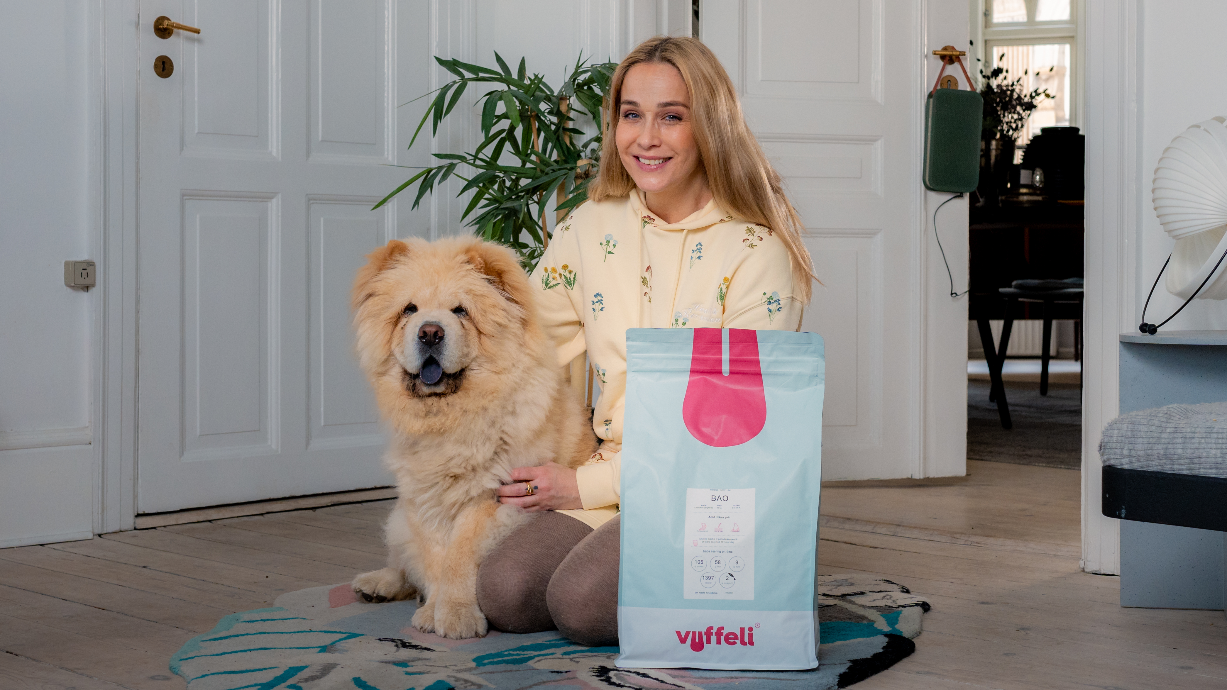 Woman showing a treat bag to a fluffy dog indoors.