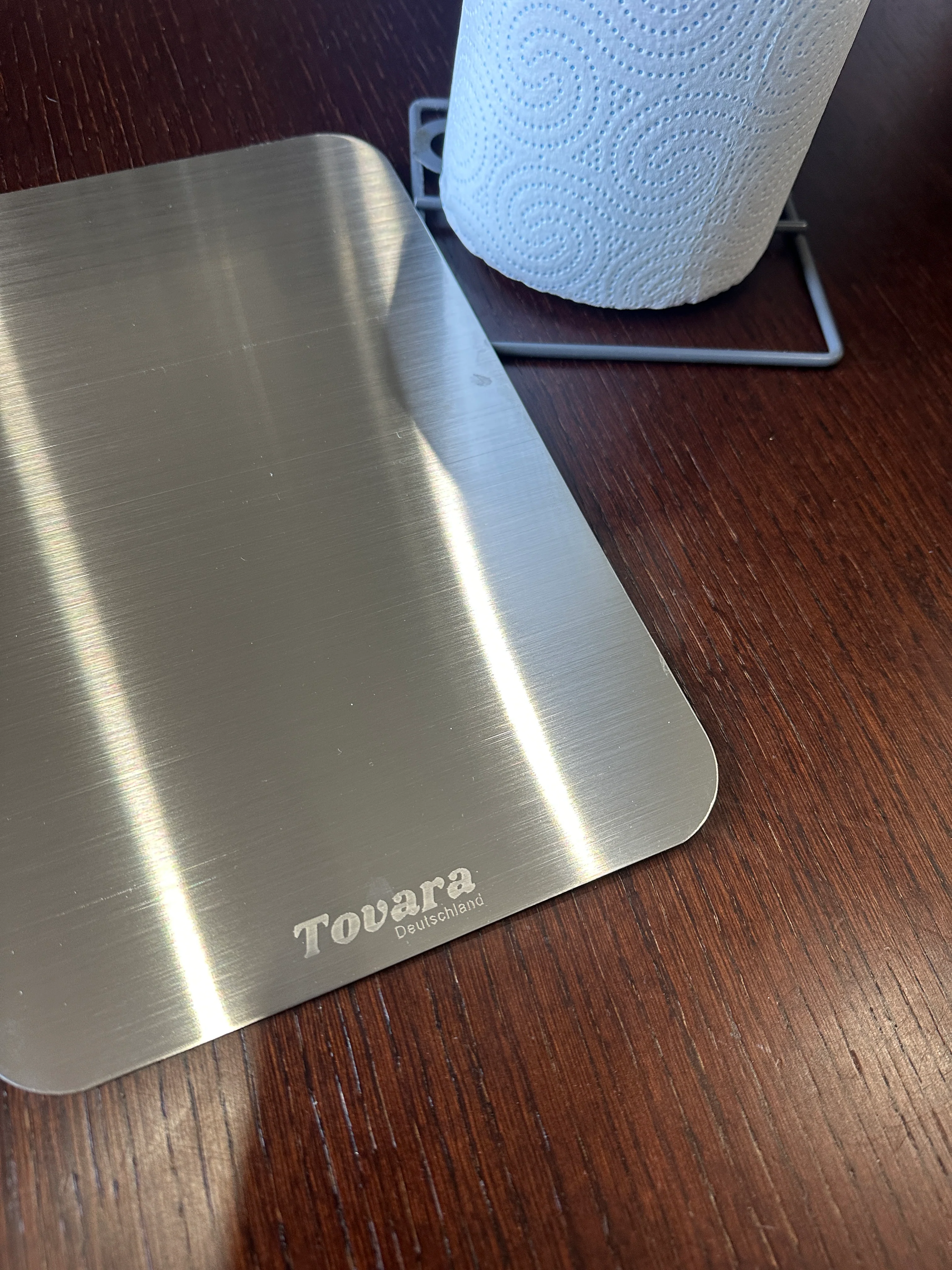 Stainless steel plate and paper towel on dark wooden surface.