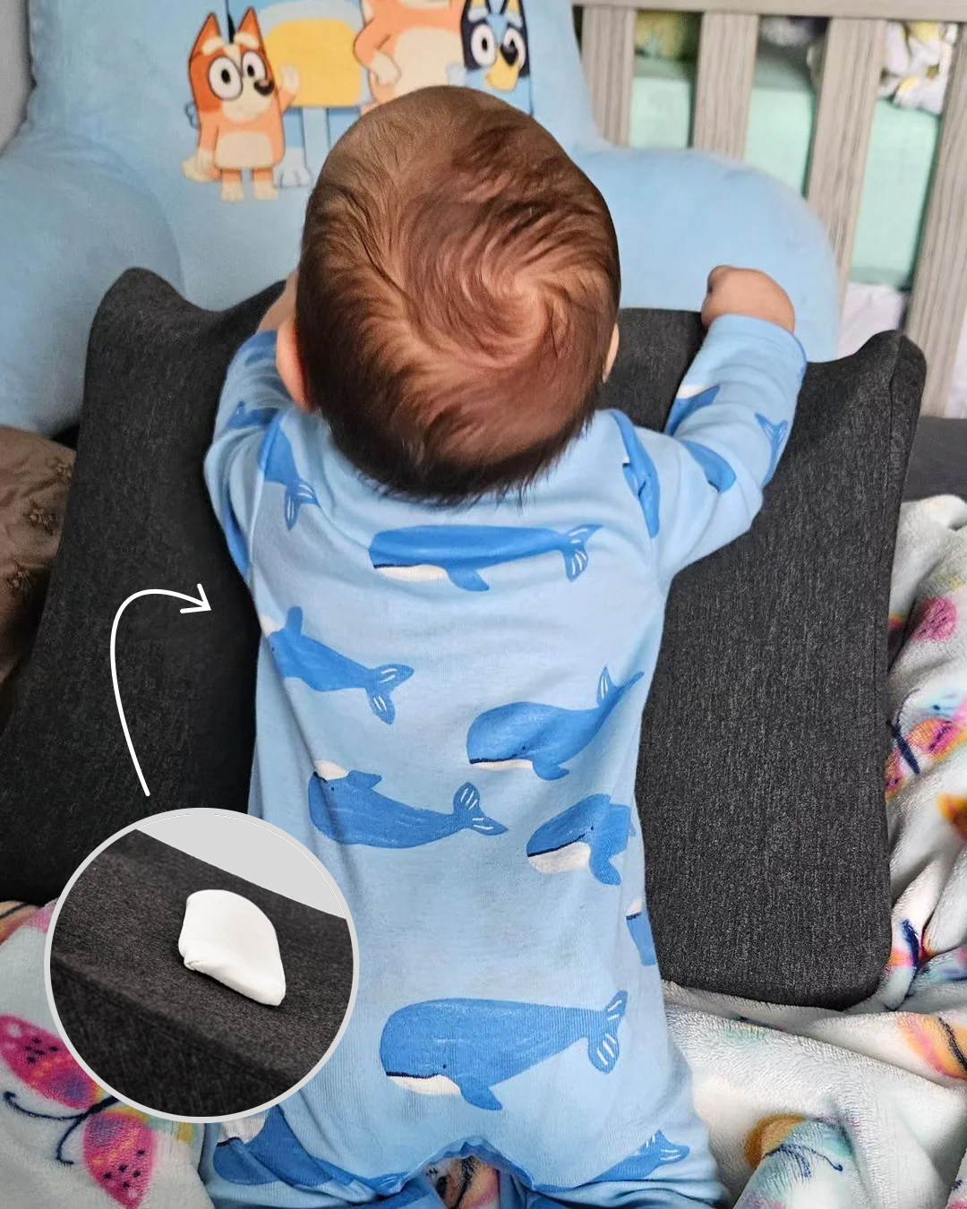 Baby in blue whale pajamas leaning on a cushion with cartoon characters.