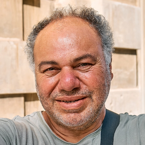 A man with short hair and a beard smiling outdoors.