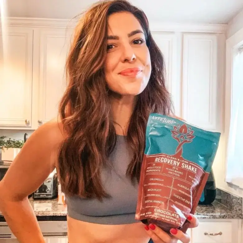 Person holding a recovery shake packet in a kitchen.