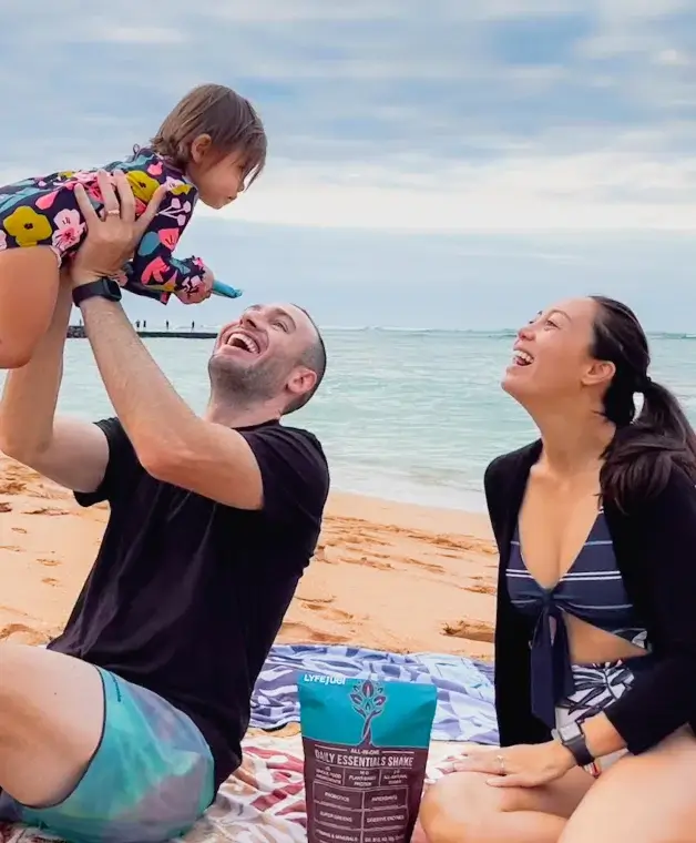 Family enjoying a beach picnic, with a man lifting a child.