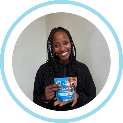 A smiling woman with long braids holds up a blue bag of Pawsitive Calming dog supplements.