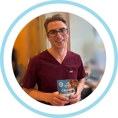 A smiling man in scrubs and glasses holds up a bag of Pawd Calming treats.