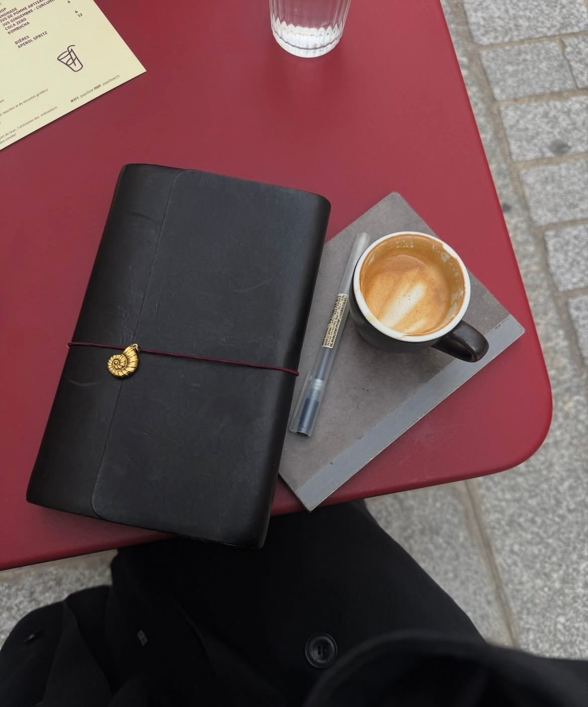 A black journal, a pen, and a cup of coffee with latte art on a red table