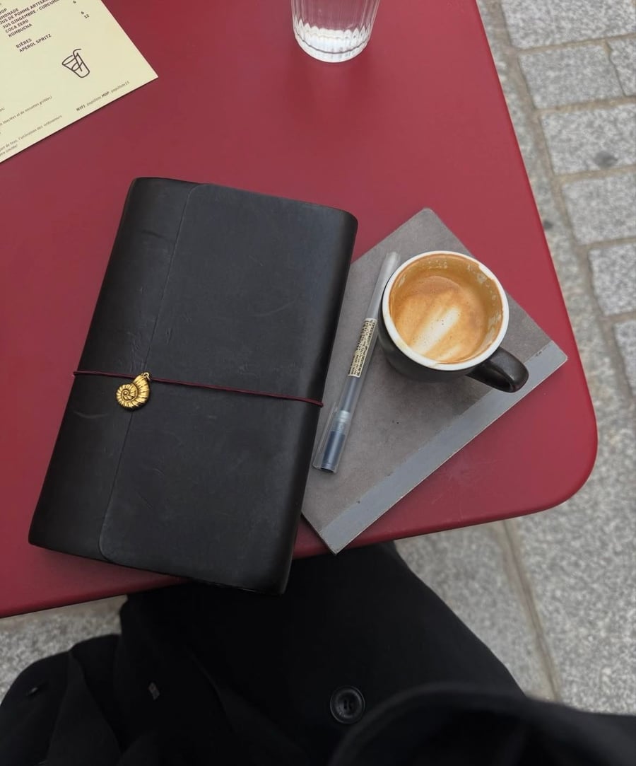 A black journal, a pen, and a cup of coffee with latte art on a red table