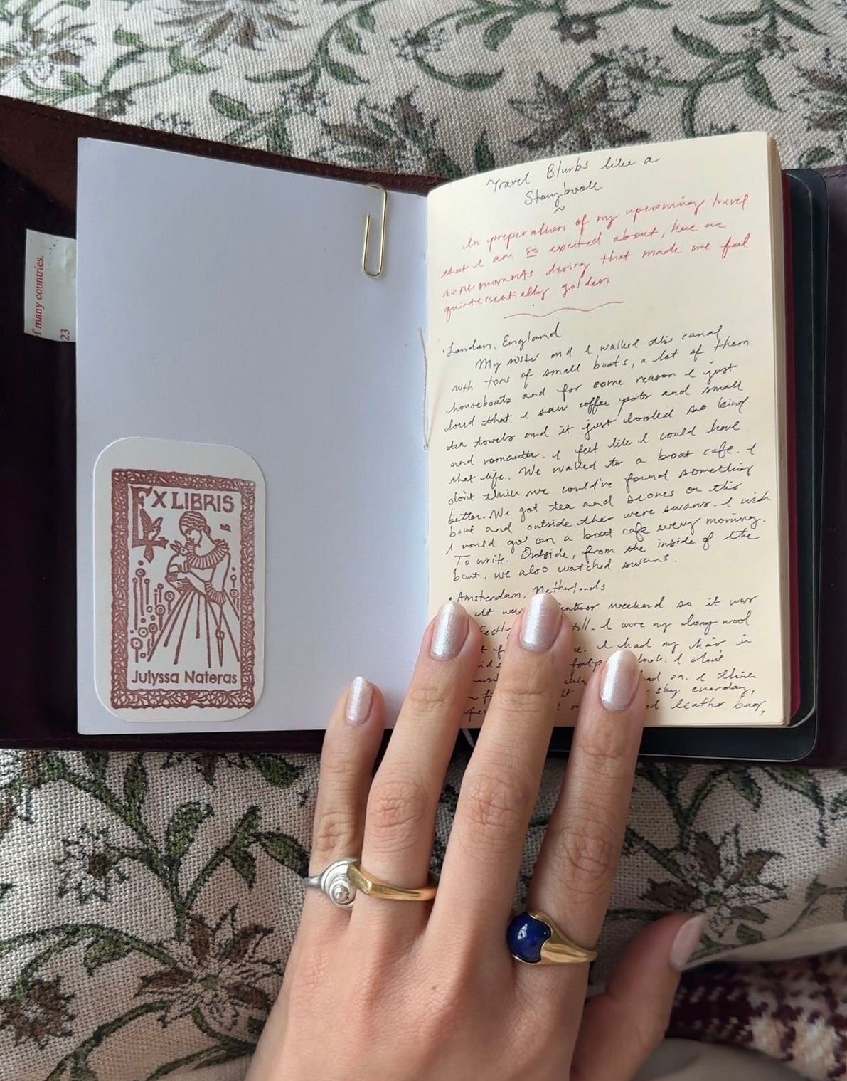 A persons hand with pearly nail polish and rings resting on an open, handwritten journal