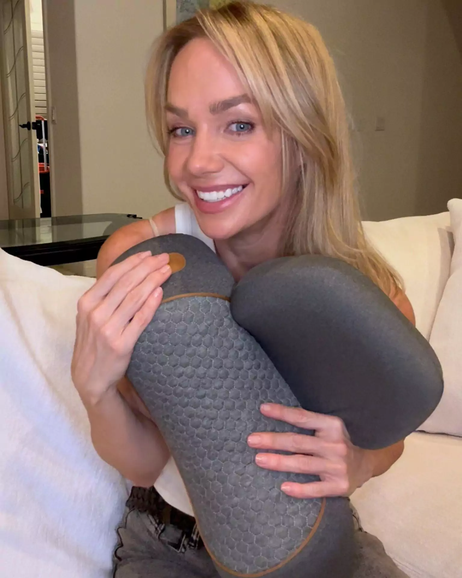 Person smiling while holding a gray, textured pillow on a couch.
