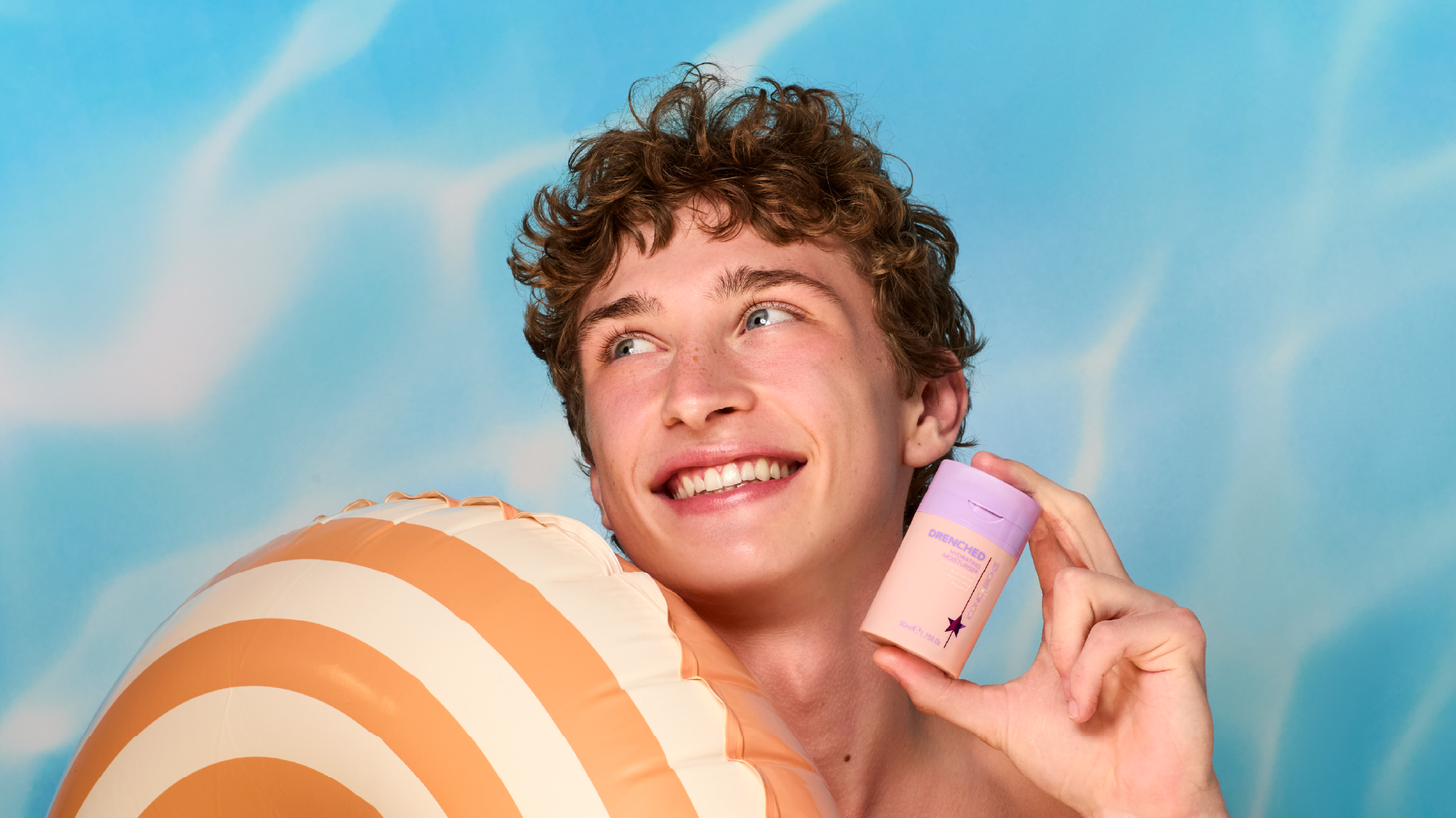 Smiling person holding a striped inflatable and a small container against a blue background.
