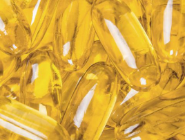 A close-up shot of many shiny, translucent, golden-yellow softgel capsules piled together.